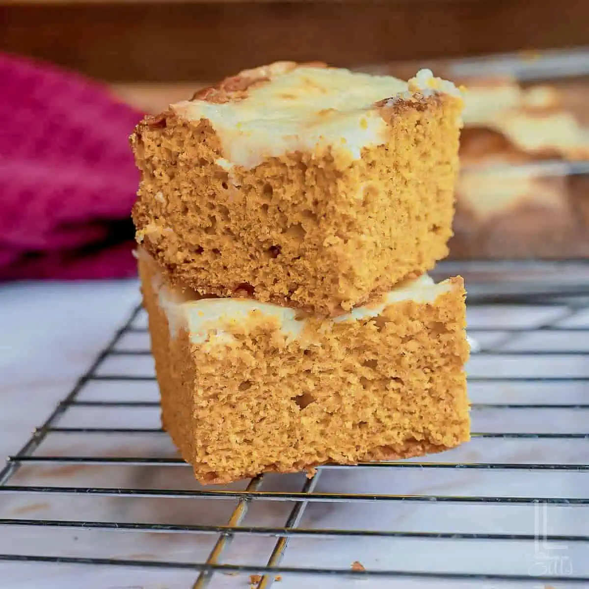 two pumpkin cake mix bars stacked on a baking rack, topped with a cream cheese swirl.