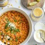 Cheesy, creamy Elote casserole with lime wedges and toppings on a wooden board.