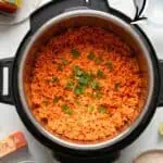 Colorful Mexican rice in Instant Pot with cilantro garnish, on a white surface.