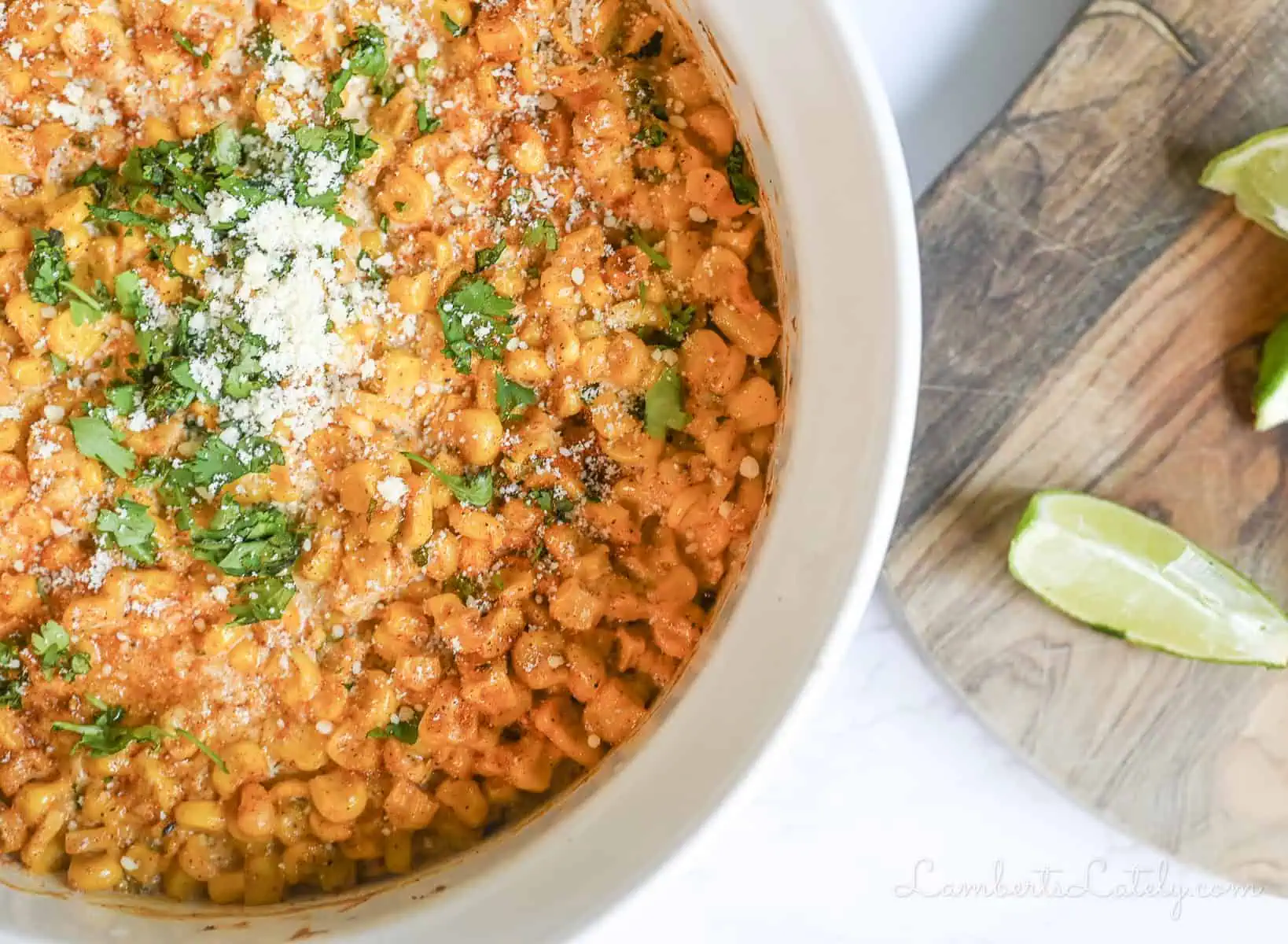 mexican street corn casserole in a dish, next to limes on a cutting board.