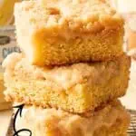Close-up of three creamy, gooey cheese chess squares stacked on a wooden surface.