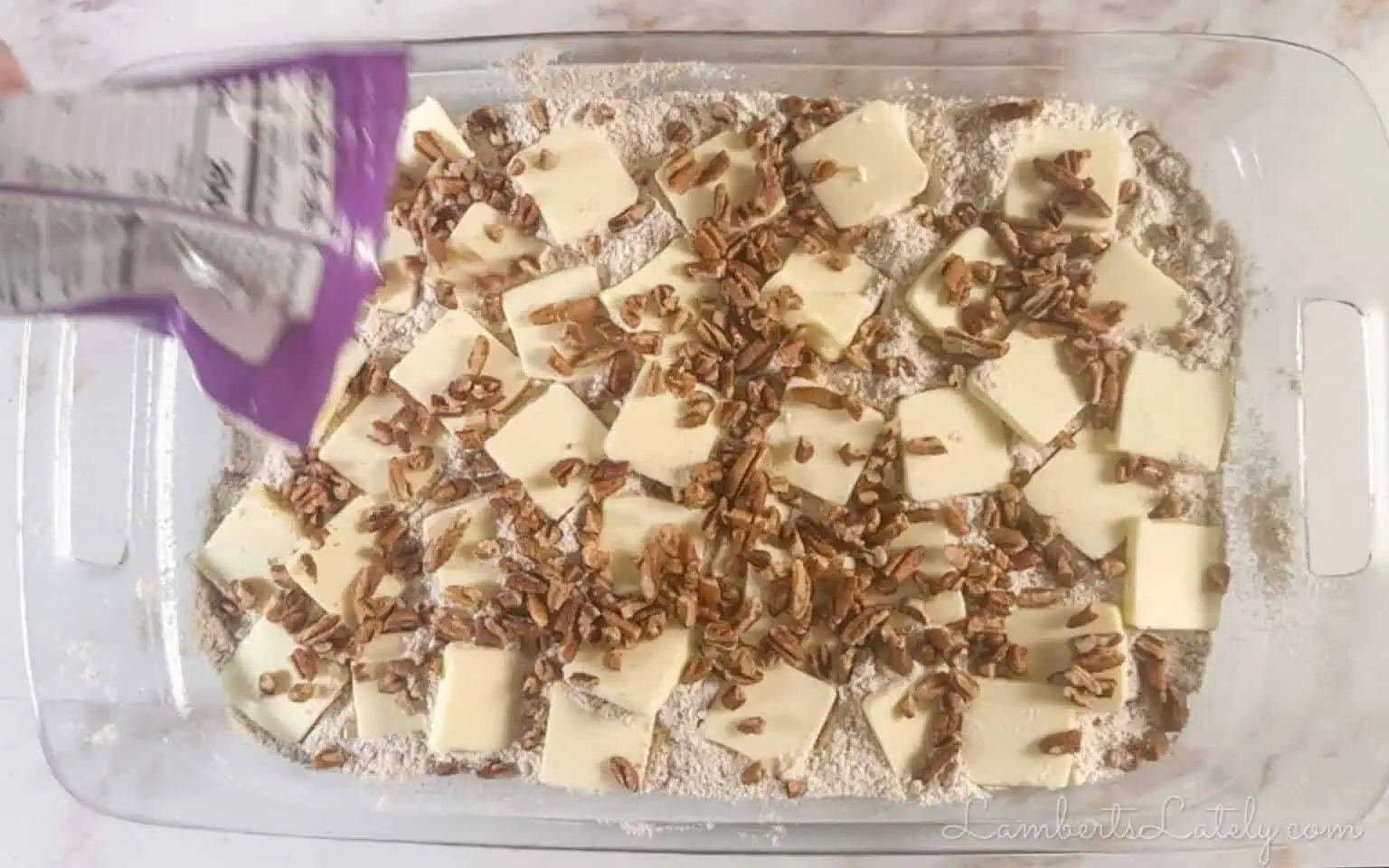 pouring pecans over butter slices in the baking dish.