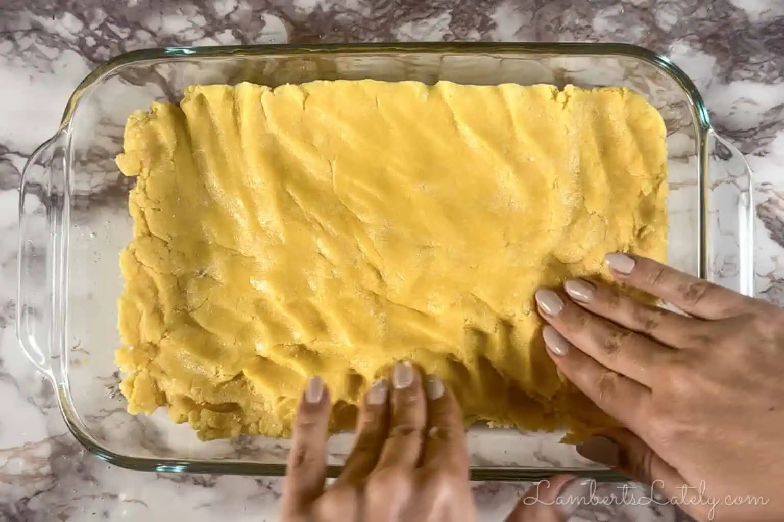 spreading cake mix layer in a baking dish with hands.