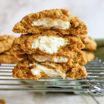 stack of pumpkin cheesecake cookies cut in half, showing cream cheese filling.