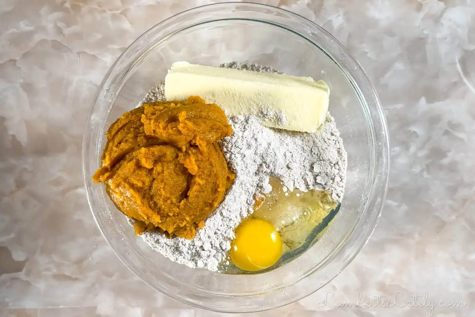 ingredients for pumpkin cheesecake cookies in a bowl; pumpkin puree, butter, cake mix, and eggs.