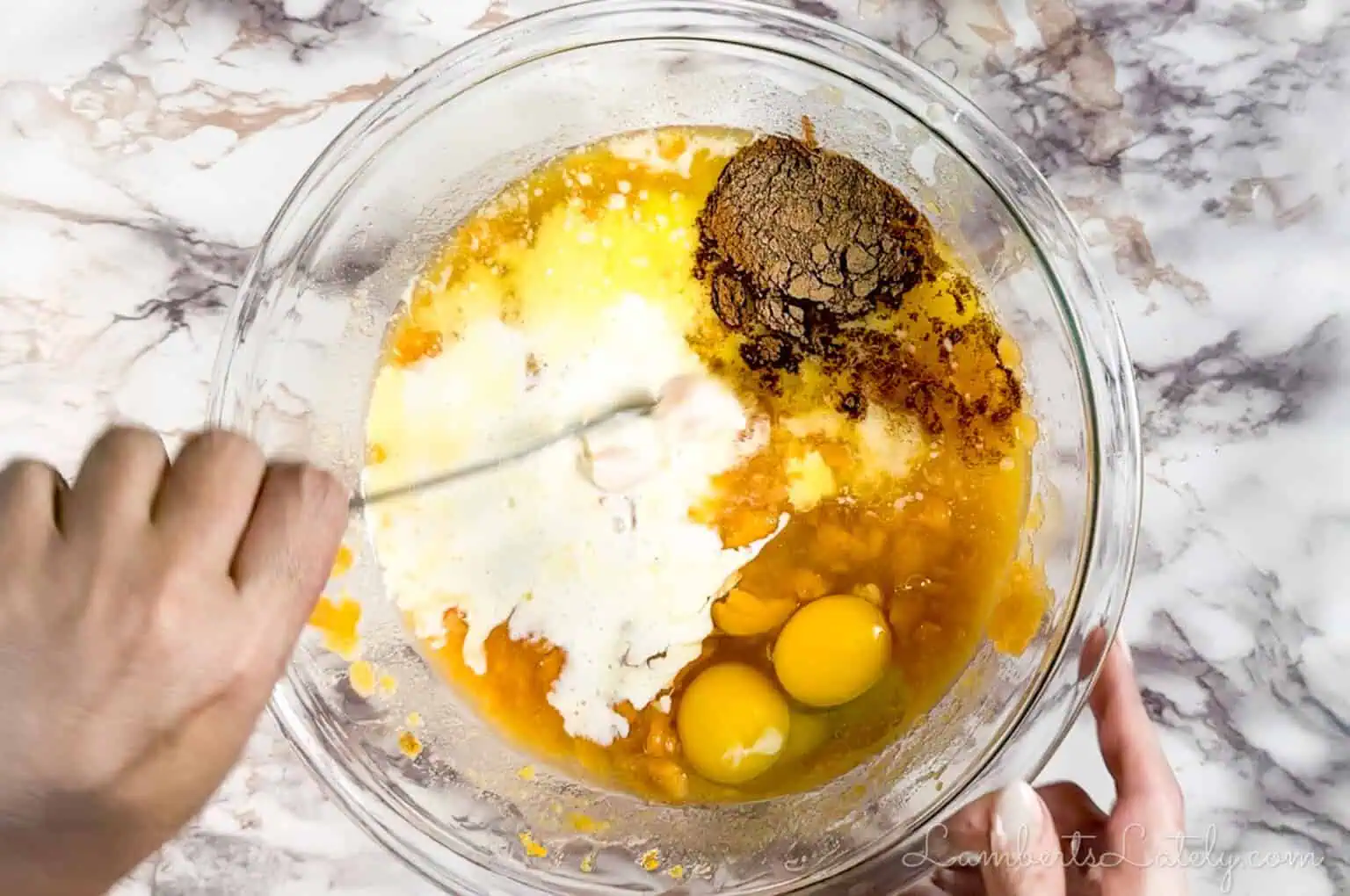stirring ingredients for sweet potato casserole in a large glass bowl.