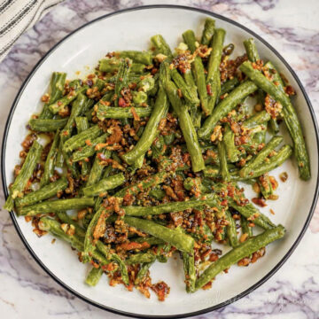 crack green beans, covered in a bacon sauce, on a plate.