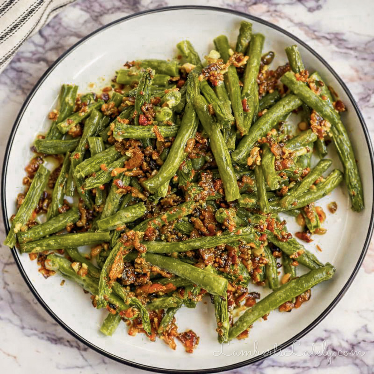 crack green beans, covered in a bacon sauce, on a plate.