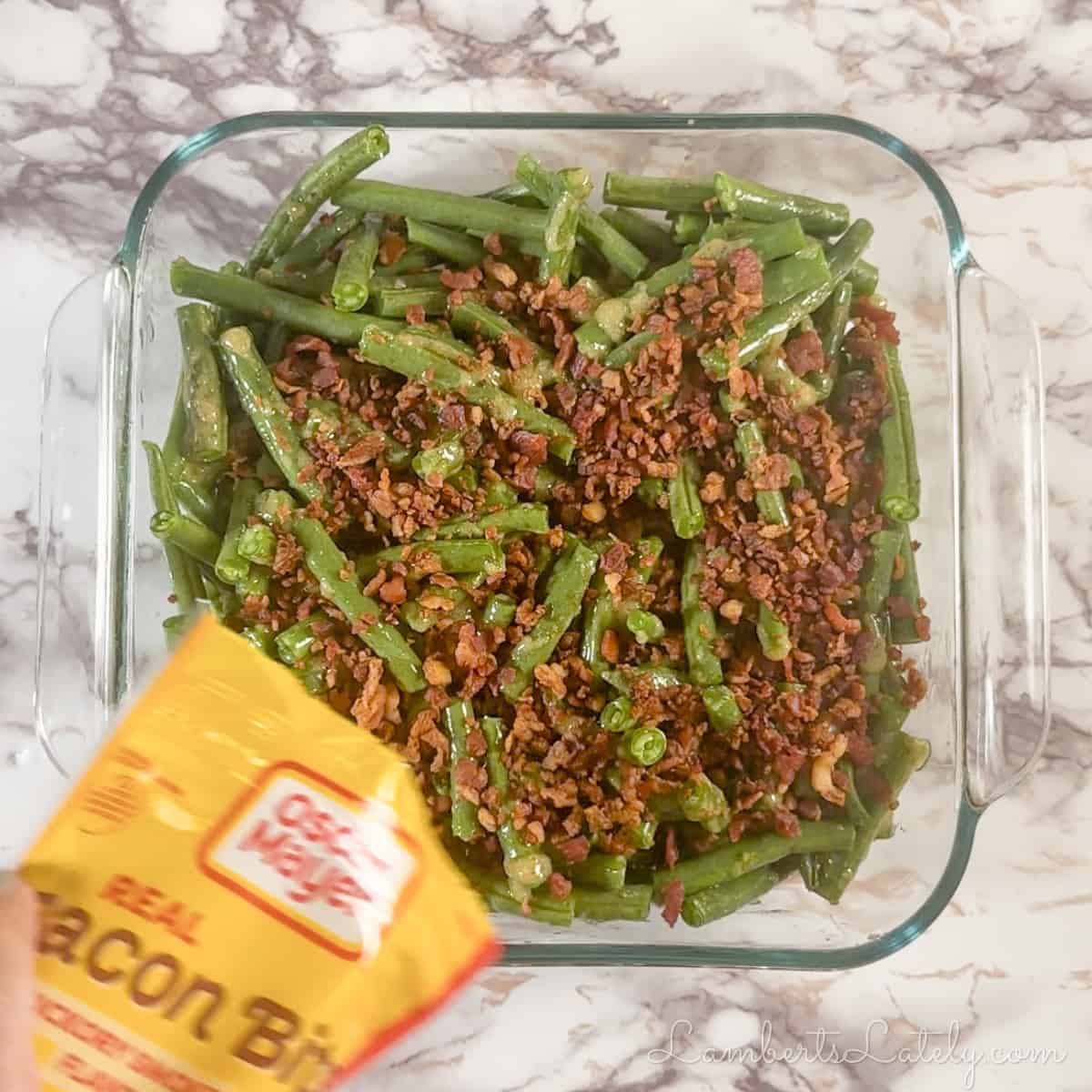 pouring bacon pieces over sauced green beans.