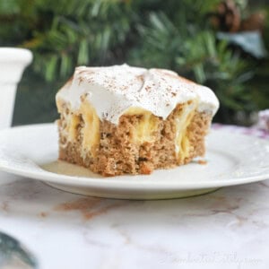 piece of eggnog poke cake on a plate in front of greenery and a baking pan.