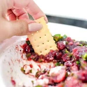 dipping a cracker into cranberry jalapeno dip.