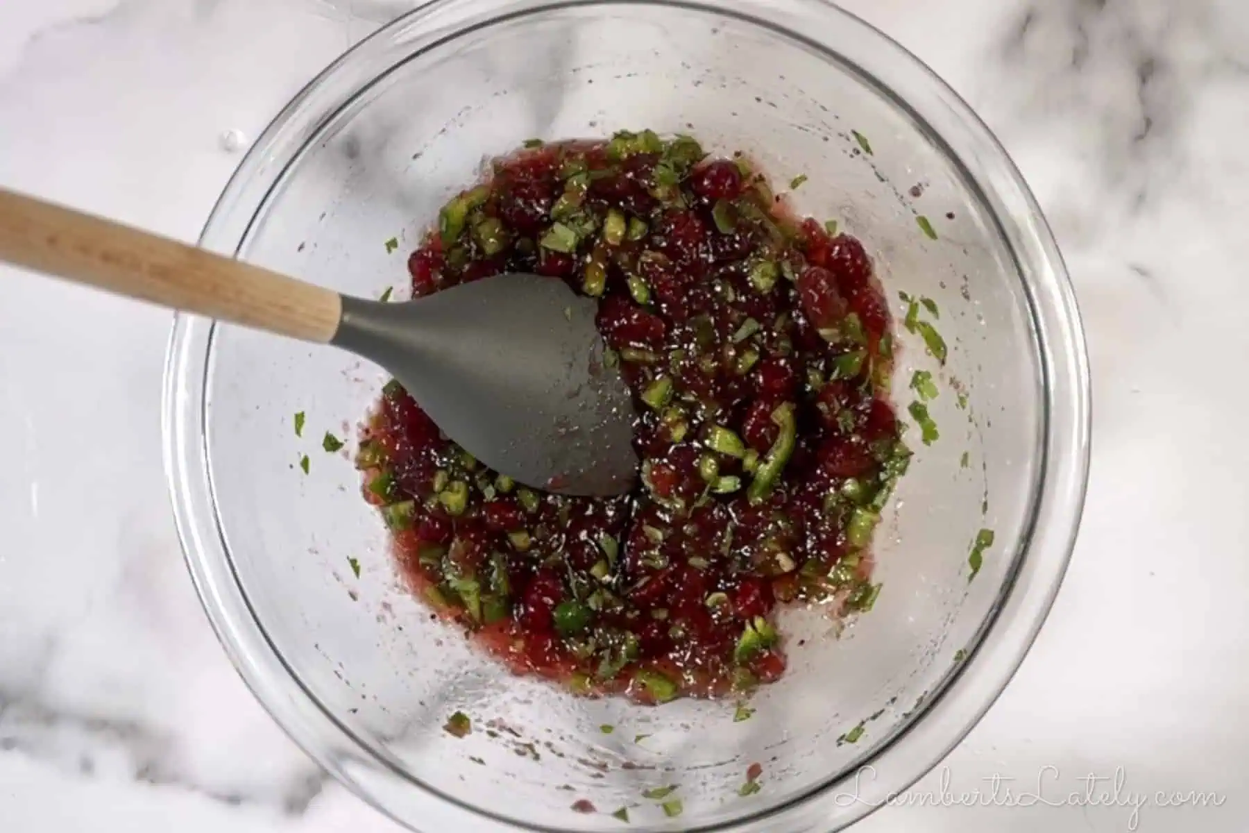 large spoon in a bowl of cranberries, cilantro, and jalapenos.