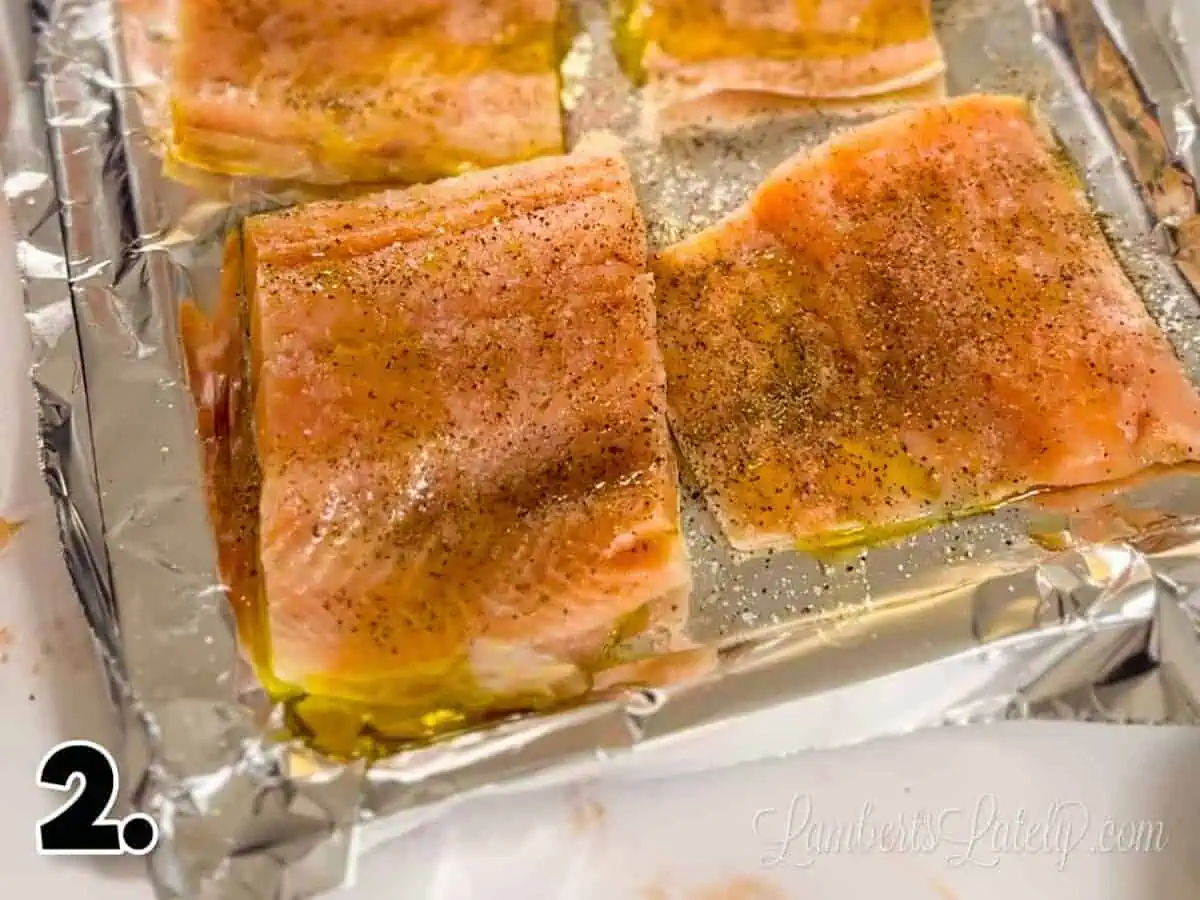 salmon fillets with olive oil, salt, and pepper on a cooking sheet.