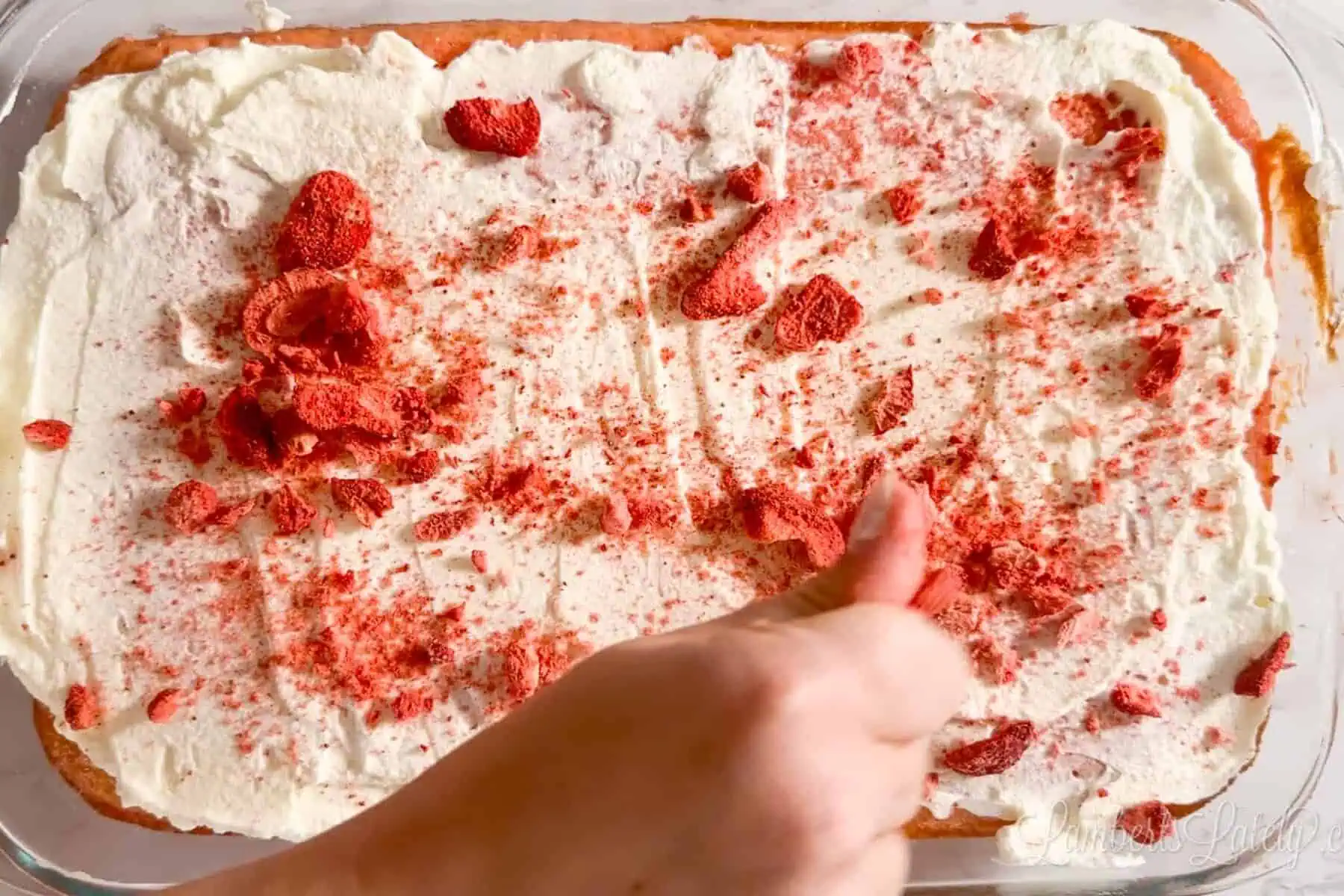 sprinkling crushed freeze dried strawberries over the tres leches cake.