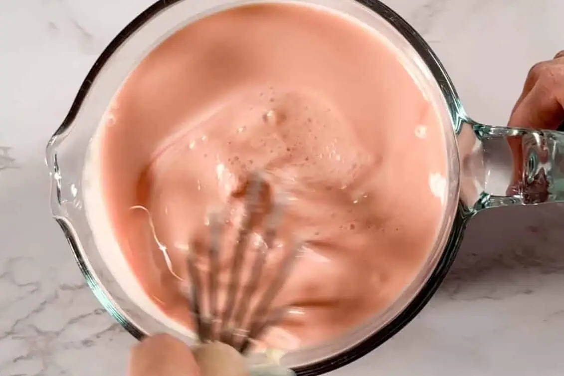 mixing strawberry tres leches mixture in a measuring cup.