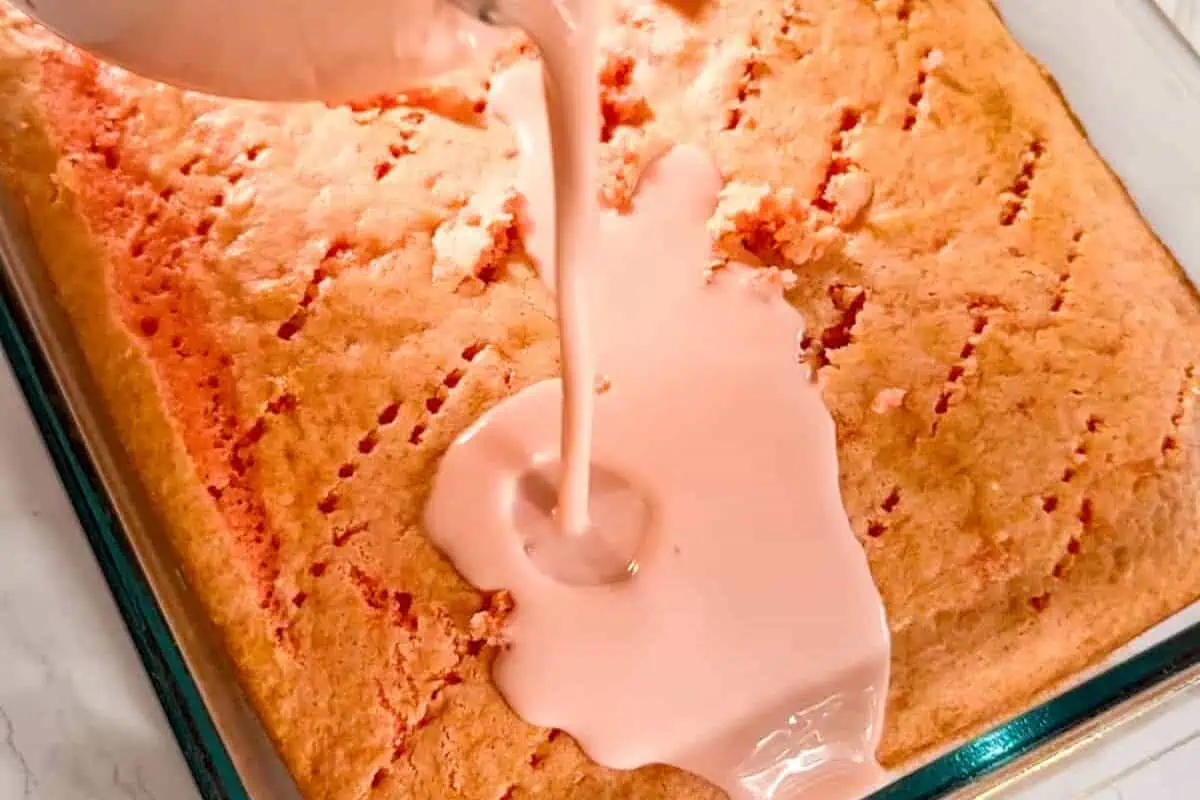pouring tres leches mixture over the strawberry cake.