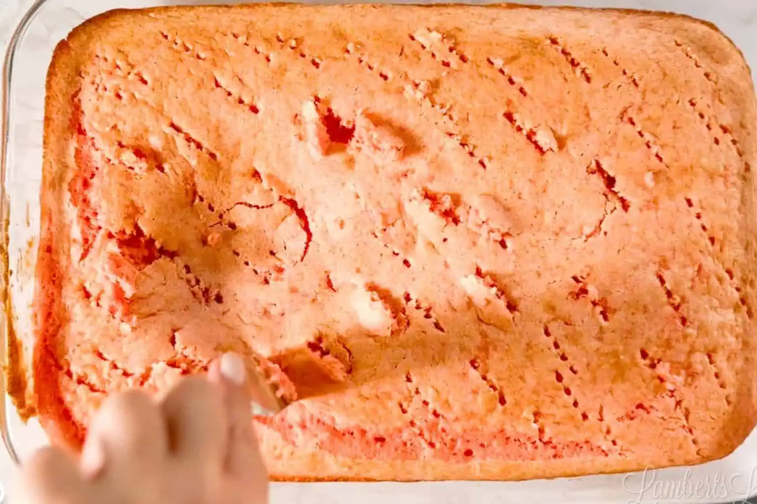 poking holes in a strawberry sheet cake with a fork.