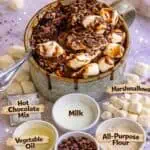 Hot chocolate mug cake with marshmallows, chocolate chips, and ingredients on a pink background.