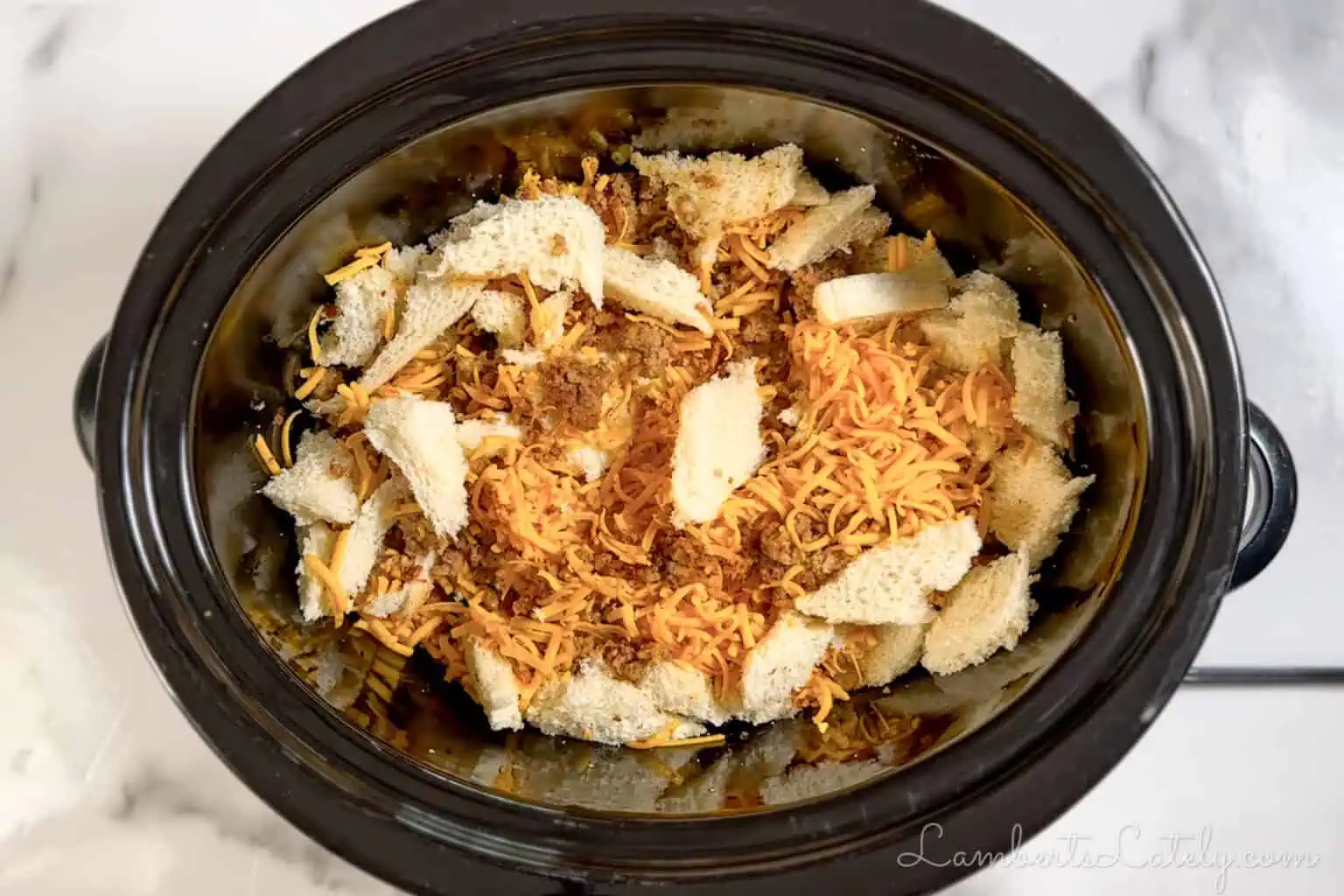 bread, cheese, and sausage mixed together in a crock pot.