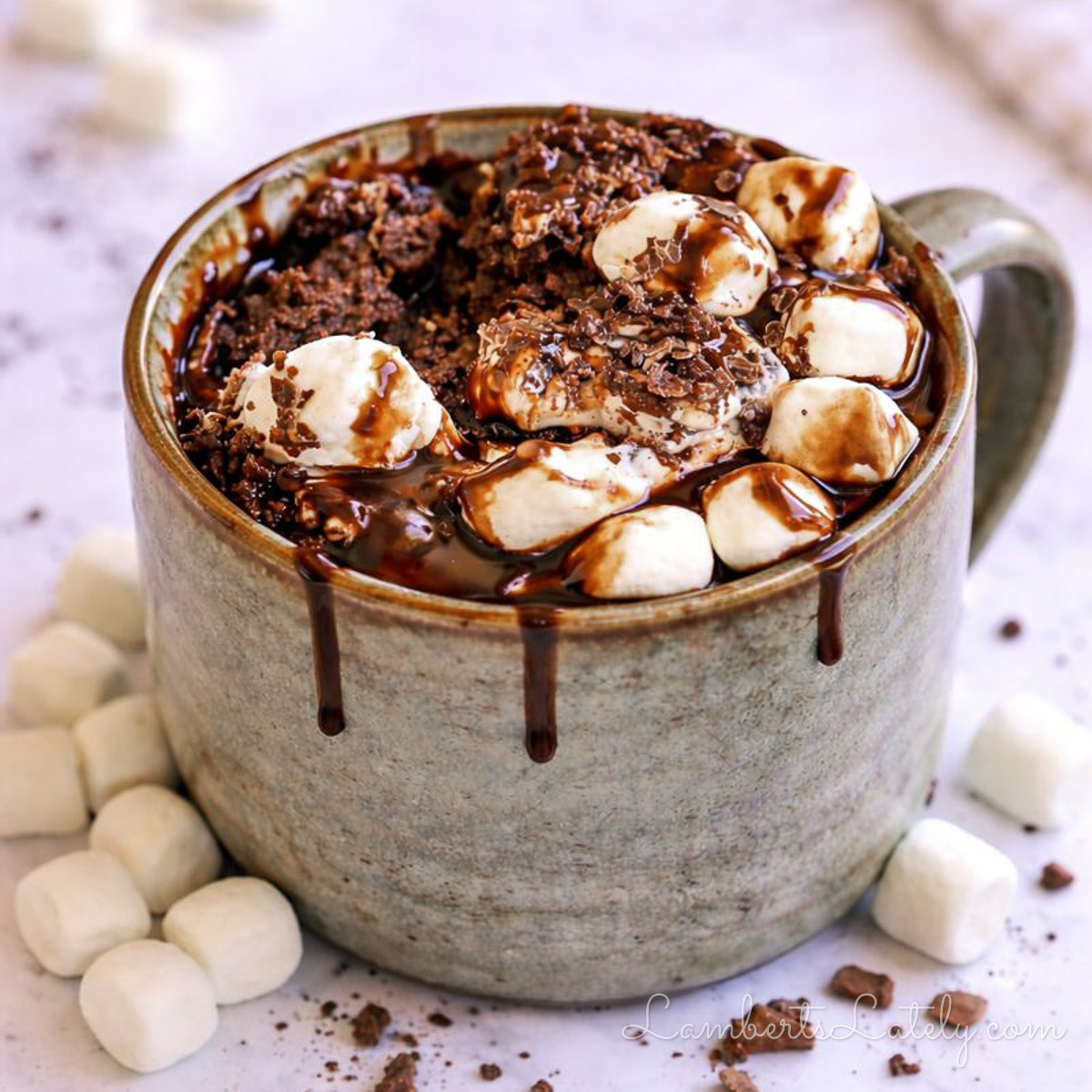 hot cocoa mug cake, covered in marshmallows and chocolate syrup, with a spoon.