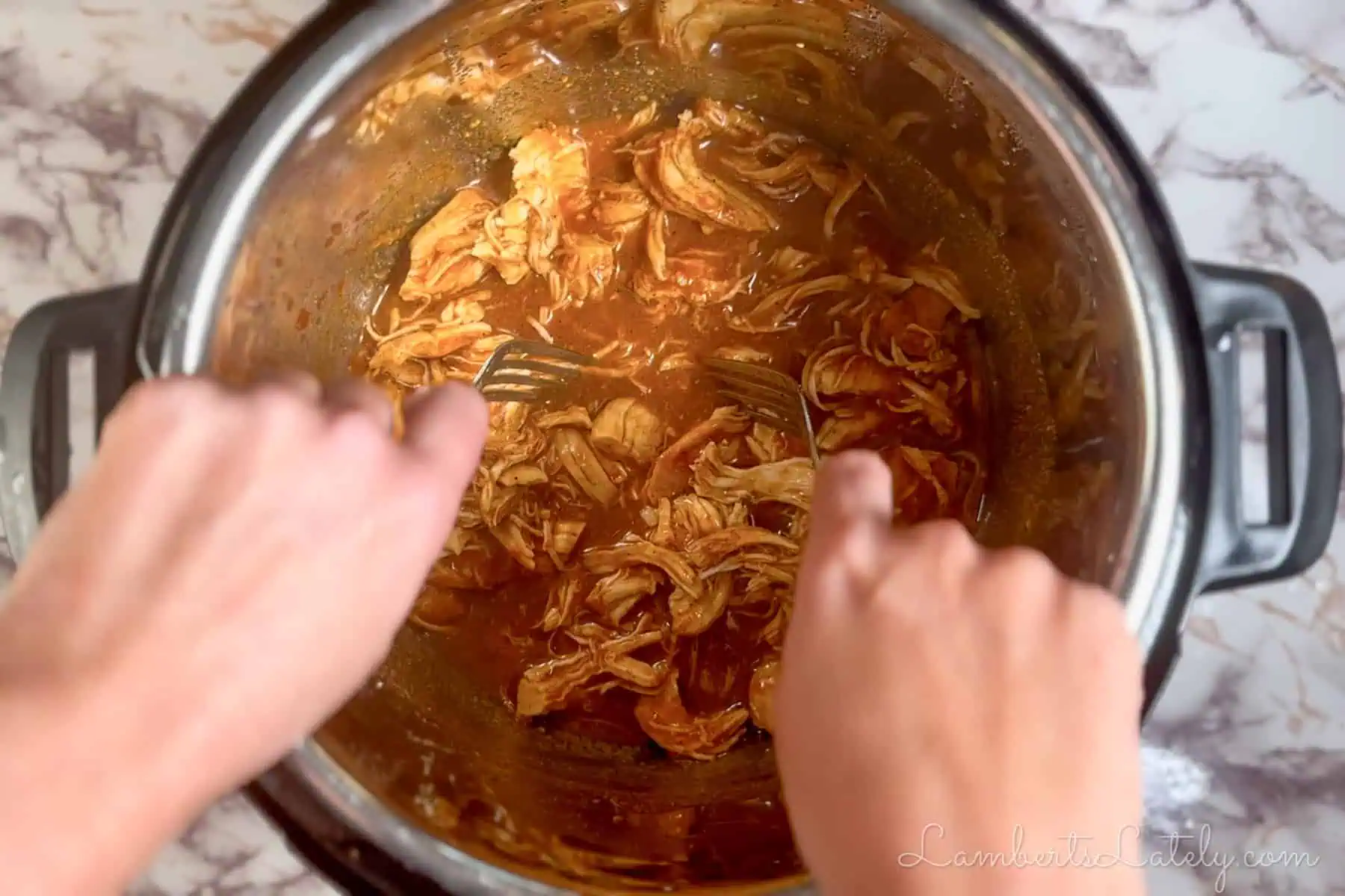 shredding cooked chicken in an instant pot with forks.