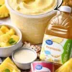 Creamy pineapple Dole Whip in a cup with pineapple slices and juice bottle.