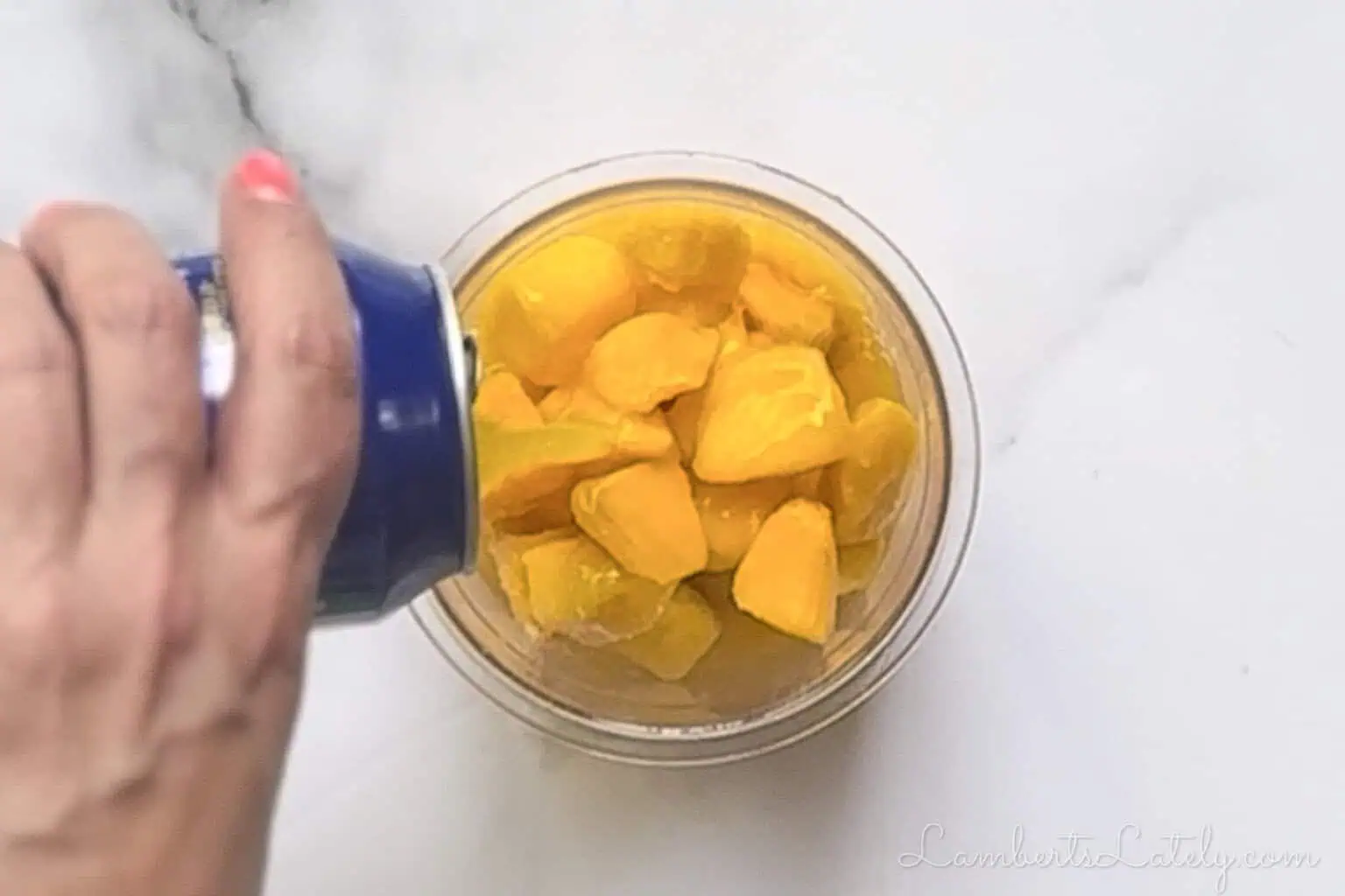 Pouring canned mango nectar into a plastic Ninja Creami pint over frozen fruit pieces.