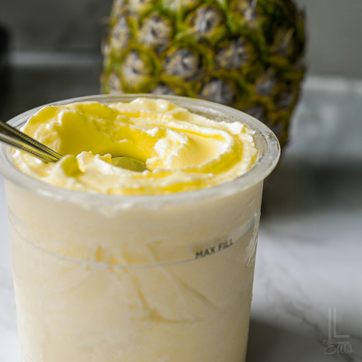 A processed pint of smooth Ninja Creami pineapple dole whip with a whole pineapple background.