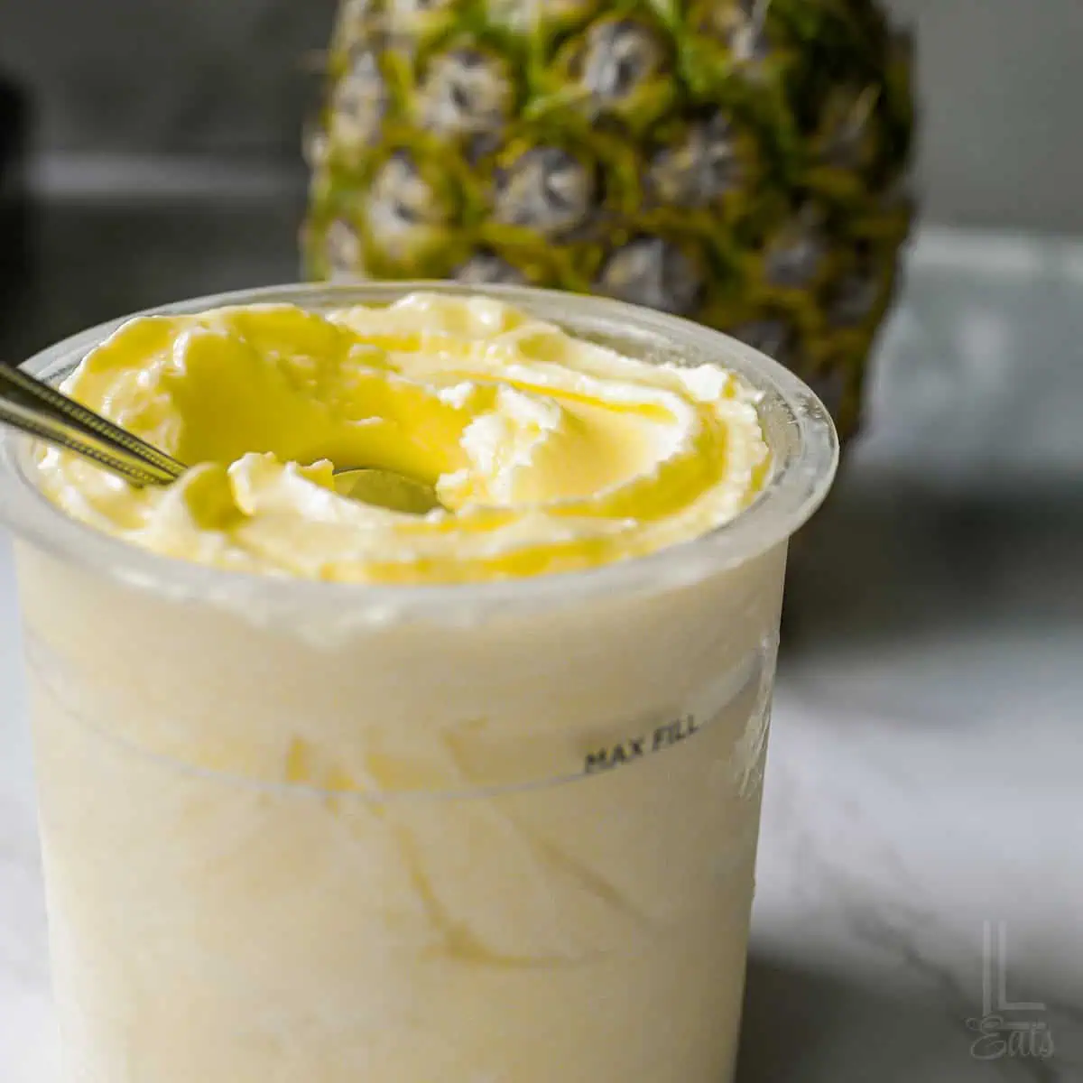 A processed pint of smooth Ninja Creami pineapple dole whip with a whole pineapple background.