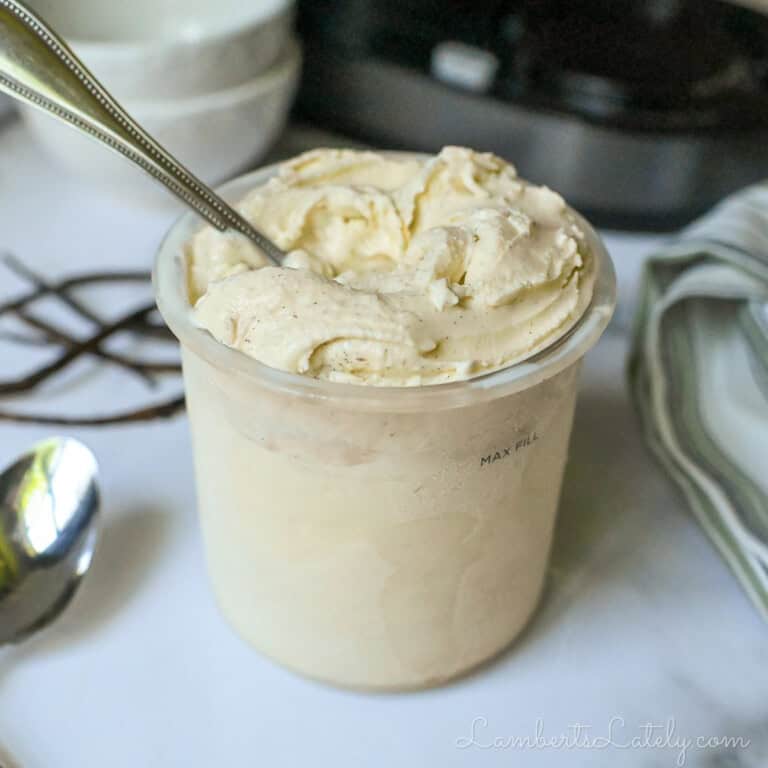 container of vanilla ice cream, with a spoon, in front of a ninja creami machine.