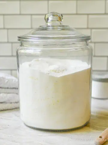 large glass jar of diy laundry deteregnt on a counter, surrounded by laundry supplies.