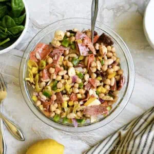 italian dense bean salad in a serving bow, surrounded by bowls, lemon, and napkin.