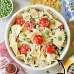 Creamy bacon pasta salad with cherry tomatoes and green peas in a white bowl.
