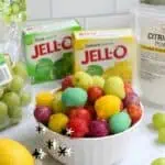 Colorful frozen sour grapes in a white bowl with lemon and Jello boxes nearby.