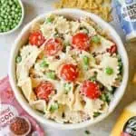 Bacon ranch pasta salad with cherry tomatoes, peas, and creamy dressing in a white bowl.