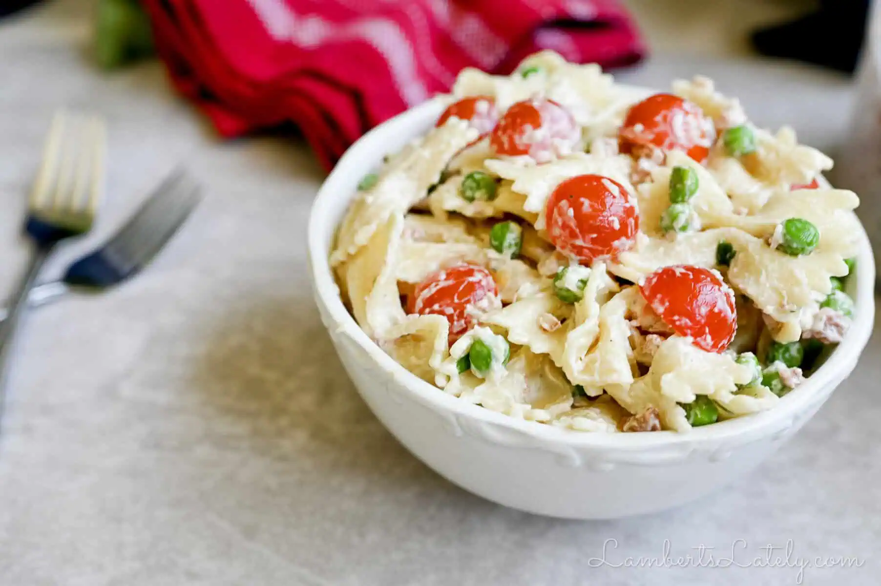 side view of a bowl of bacon ranch pasta salad, topped with tomatoes and peas.