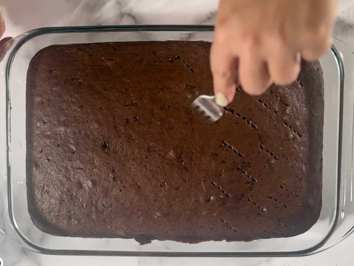 poking holes in a chocolate sheet cake with a fork.