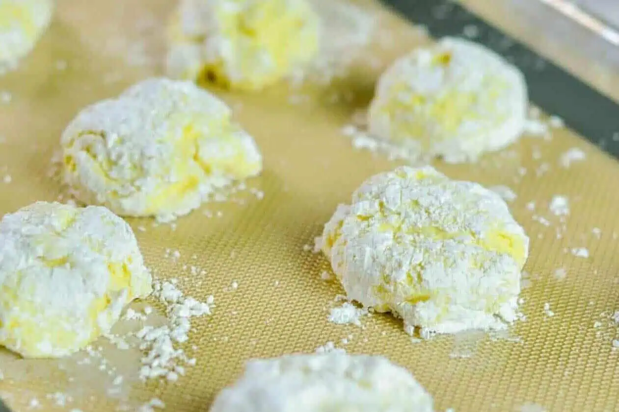 Unbaked lemon Cool Whip cookies on a lined baking sheet, after rolling in powdered sugar.