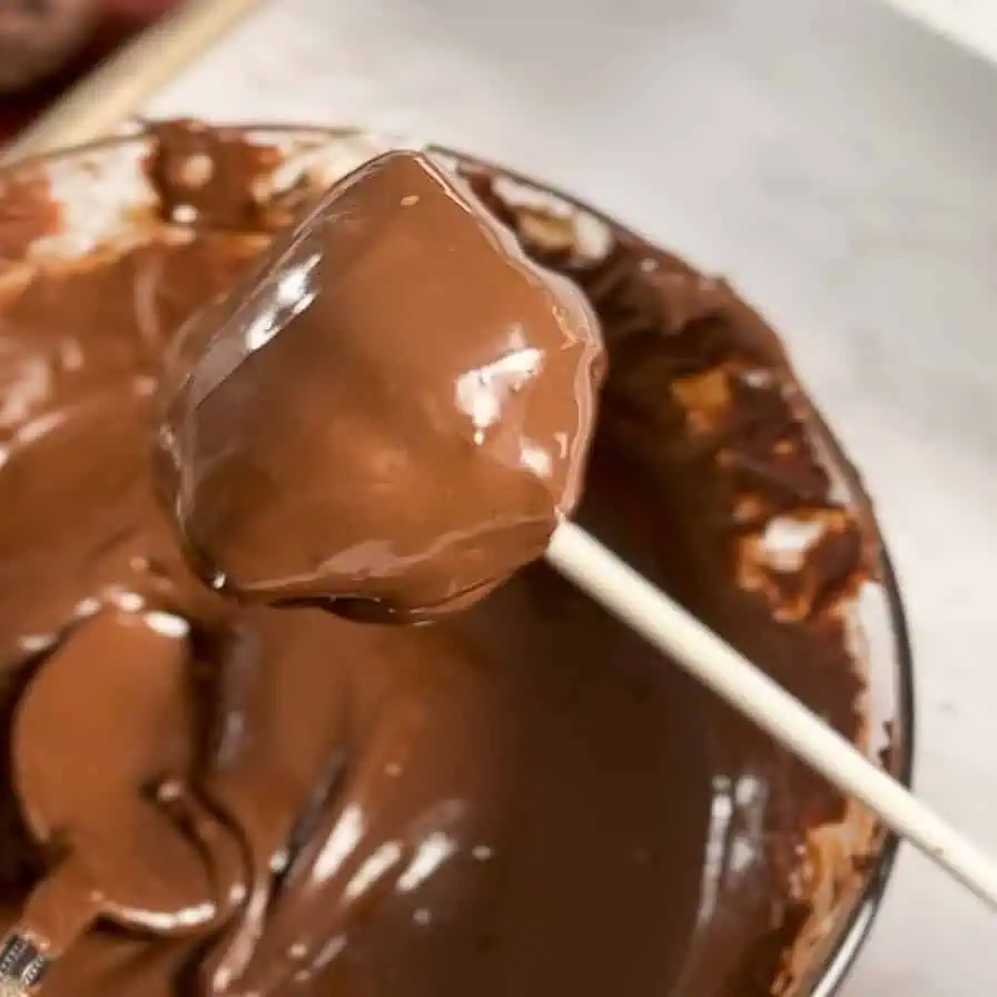 dipping a cake pop in melted chocolate.