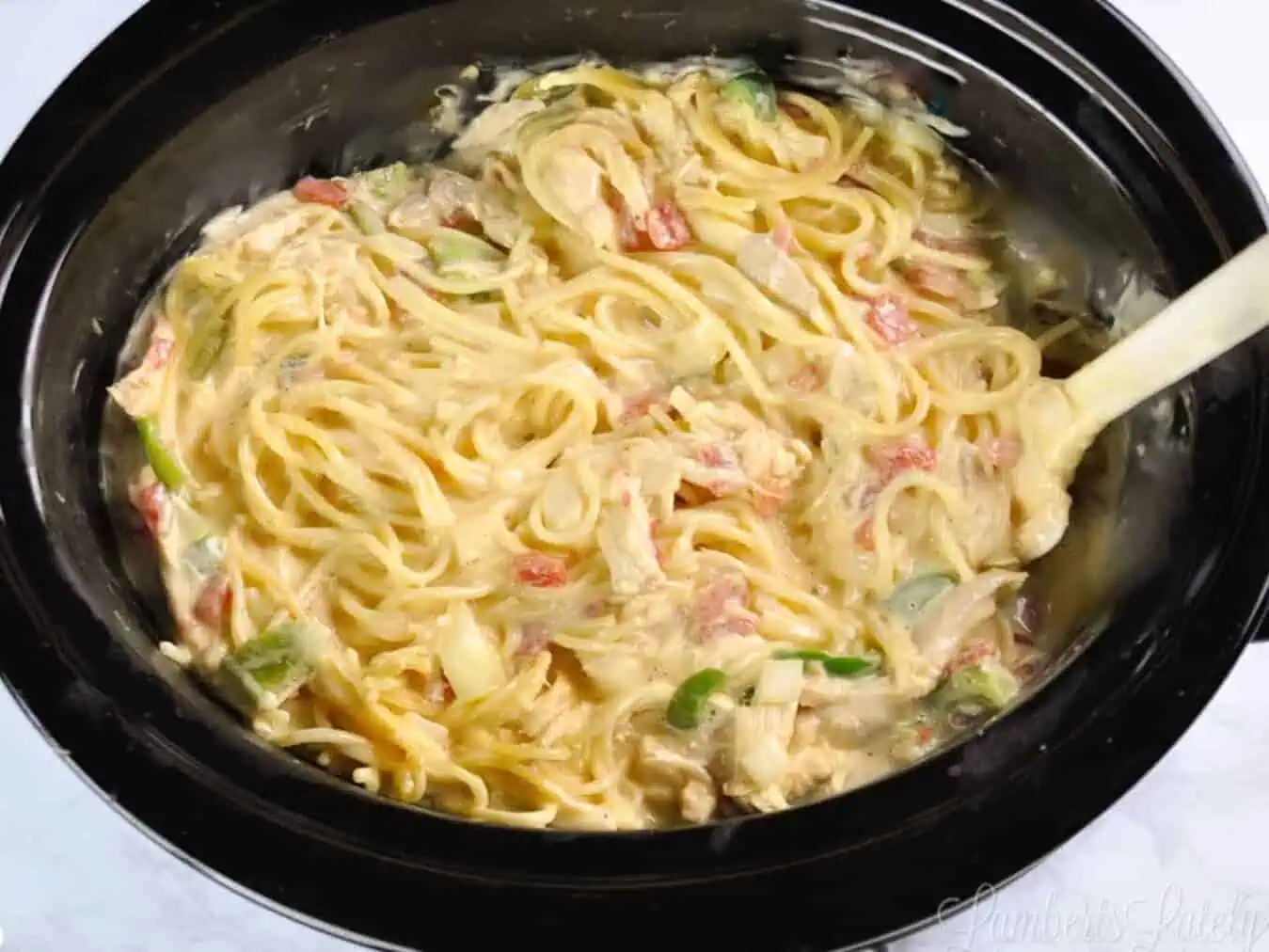 spaghetti noodles added to cheese sauce mixture in a crock pot.