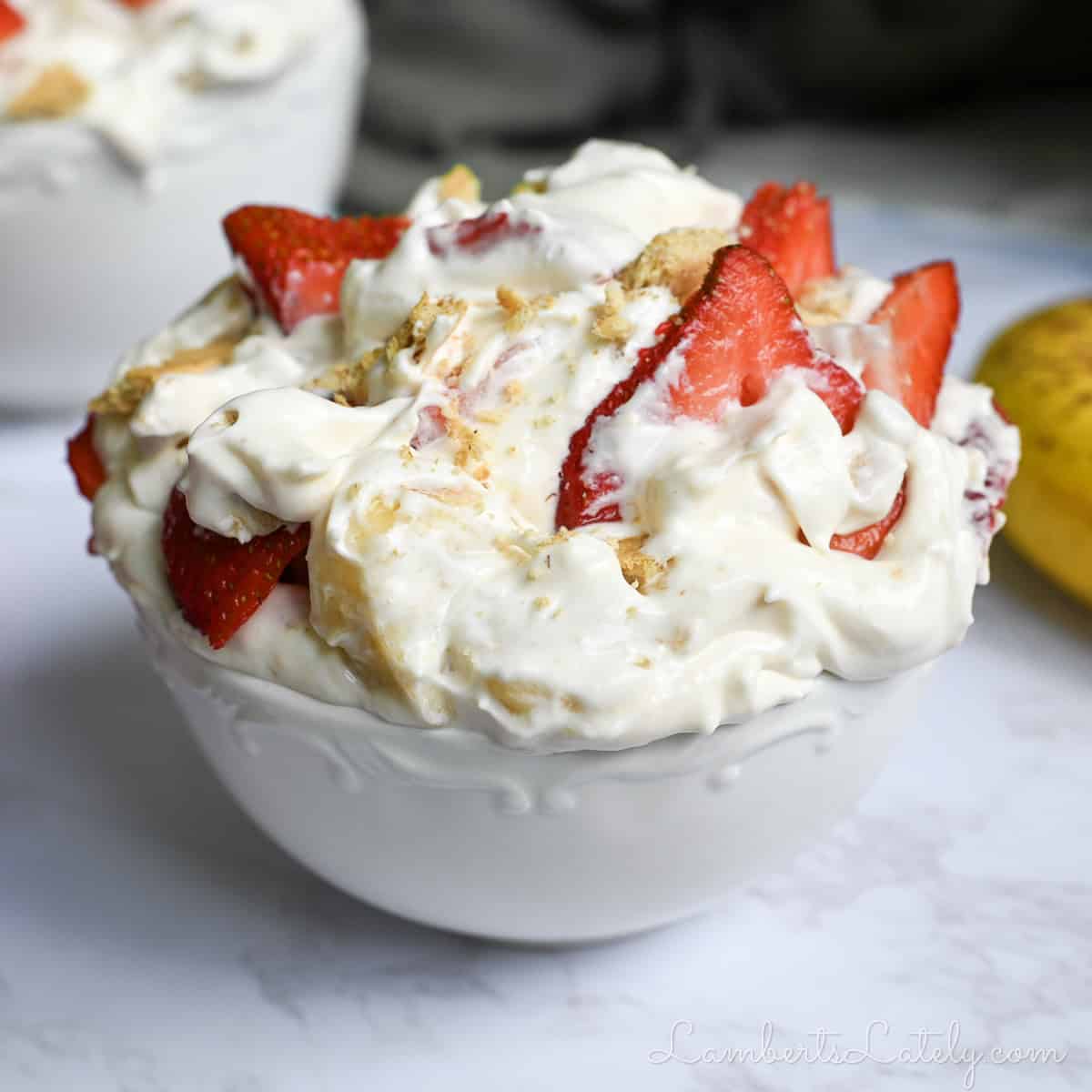 a bowl of strawberry banana cheesecake salad in front of other bowls, a banana.