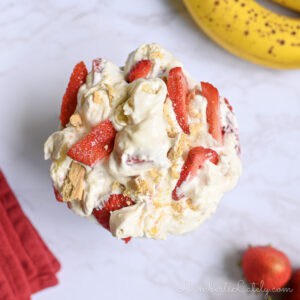 a bowl of strawberry banana cheesecake salad next to bananas, strawberries, a napkin.