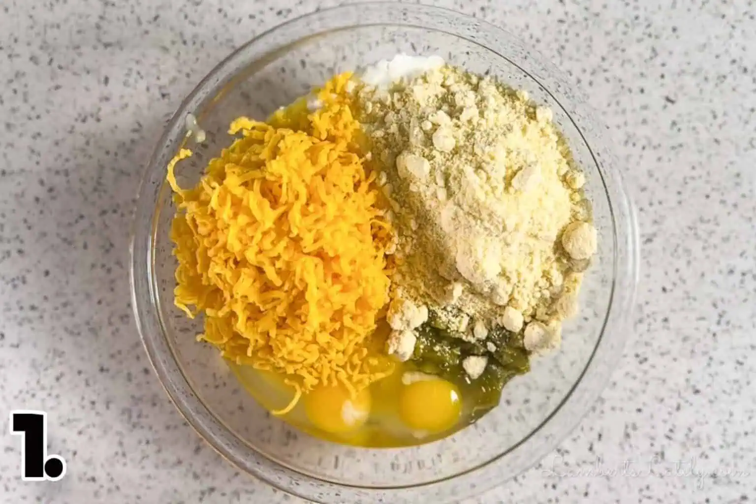 ingredients for corn casserole (jiffy mix, shredded cheddar, eggs, green chilies) in a bowl before mixing.