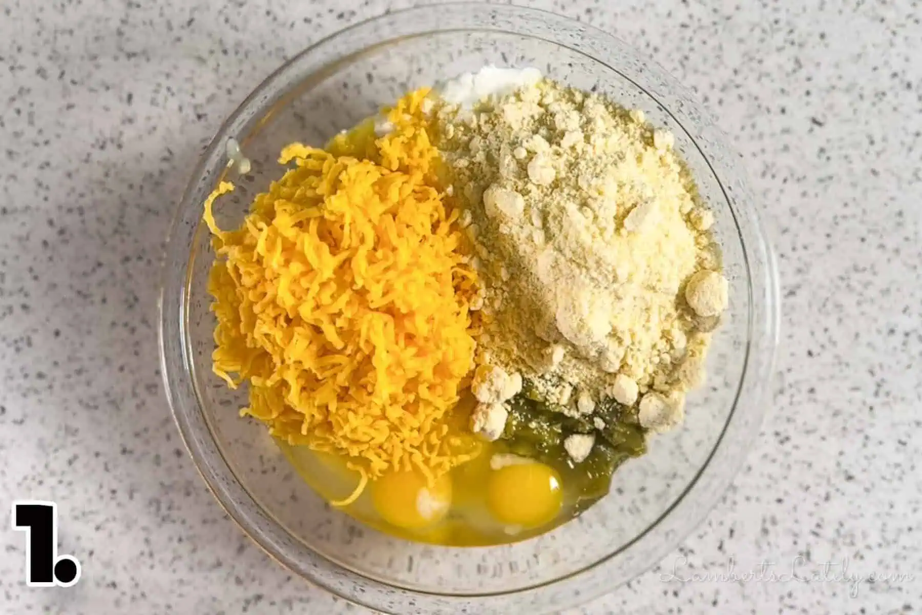 ingredients for corn casserole (jiffy mix, shredded cheddar, eggs, green chilies) in a bowl before mixing.