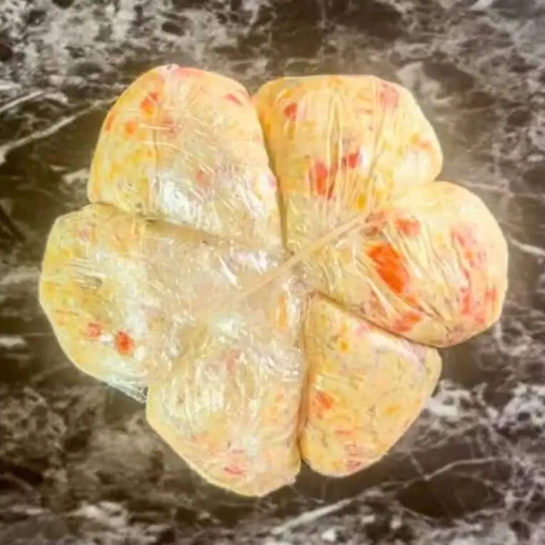 cheese ball wrapped in plastic wrap and rubber bands.