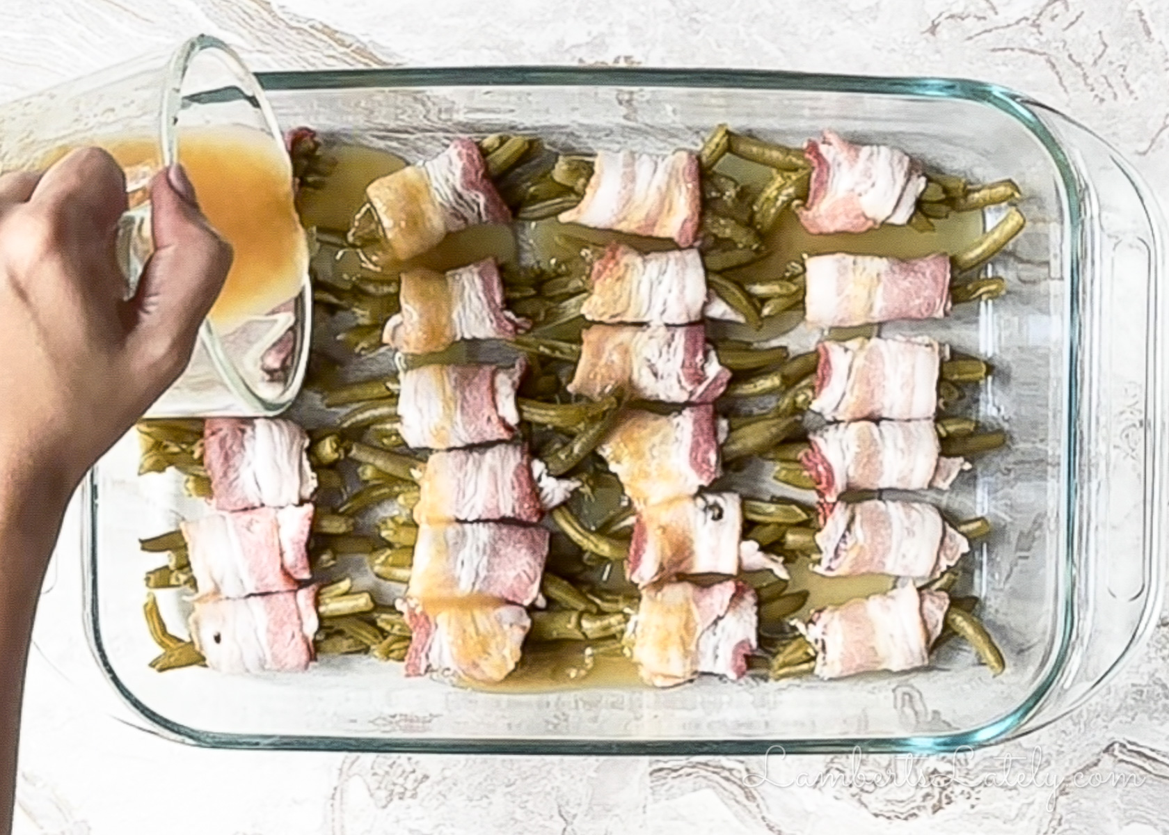 pouring butter brown sugar mixture over the rolled green bean bundles before baking.