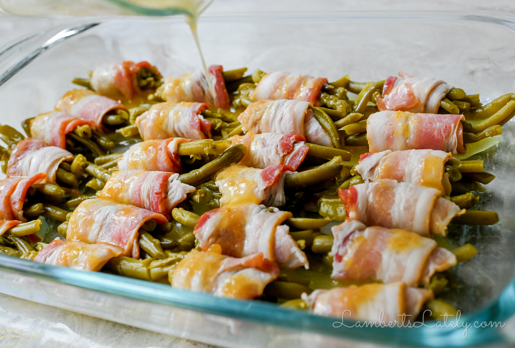 pouring brown sugar butter glaze over bacon wrapped green bean bundles.