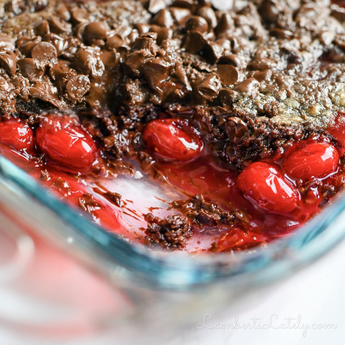 looking into a pan of cherry chocolate dump cake with a serving missing, showing cherries and melted chocolate.