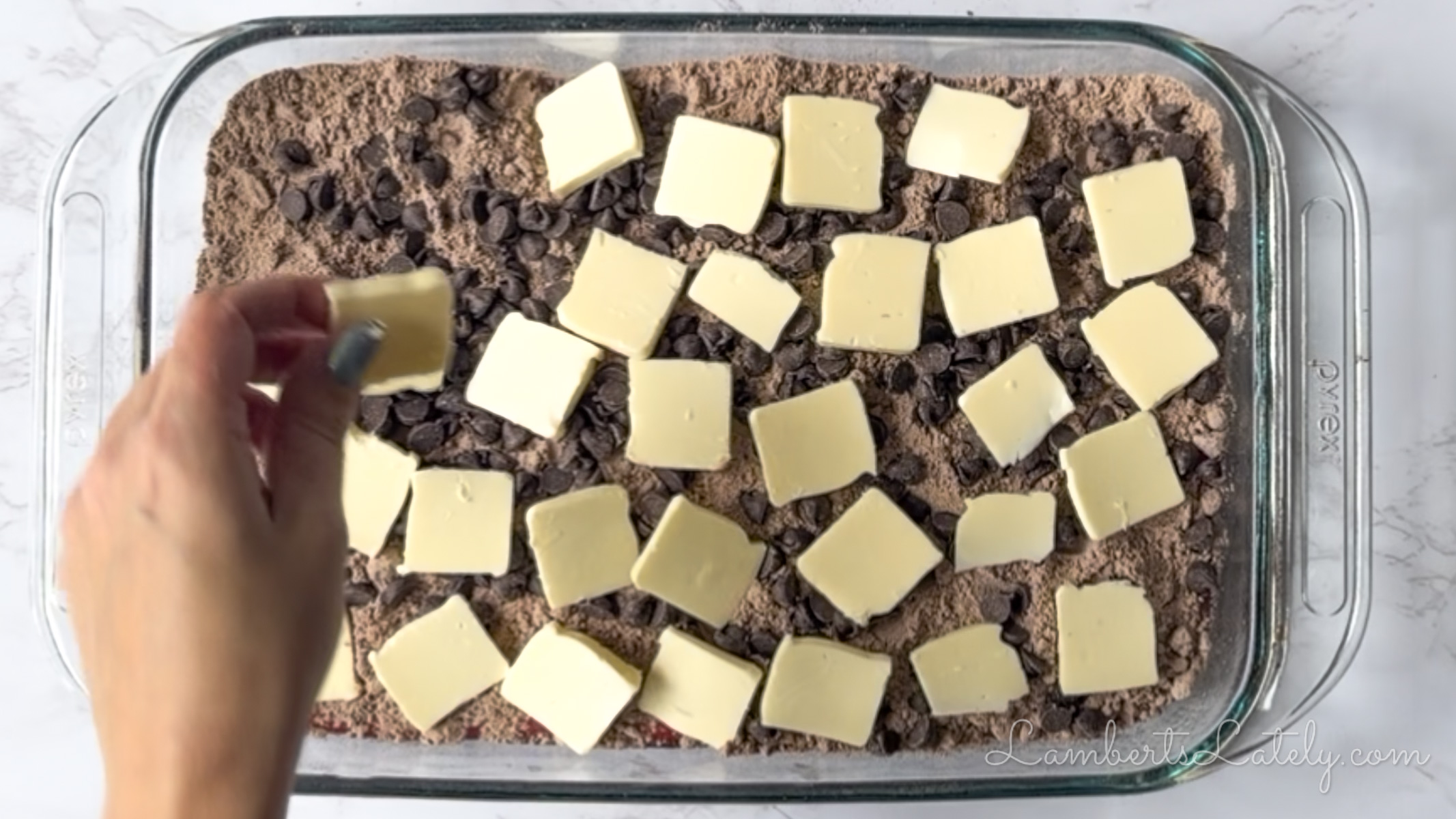 putting butter pats over cake mix and chocolate chips in a baking dish.