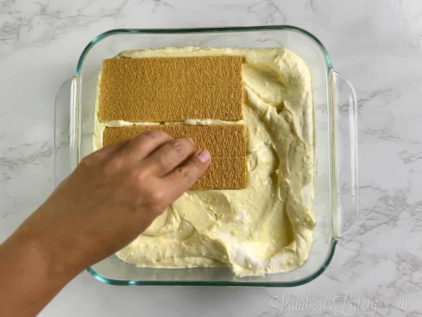 placing graham crackers over pudding mix in a square baking dish.